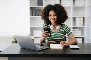  Güzel Afrikalı kadın çalıştığı yerde bilgisayarını ve telefonunu kullanıyor. Ofise odaklanmış.