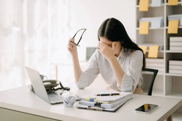 stock image Asian woman feeling migraine head strain.Overworked businesswoman financier while working on laptop at office.