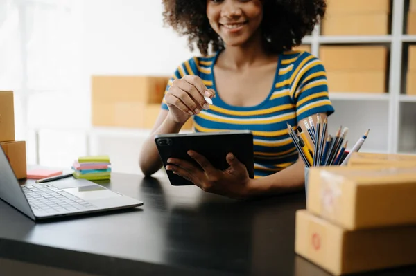 stock image Young woman holding tablet showing payment success and credit card with yellow parcel box as online shopping concept  in home office