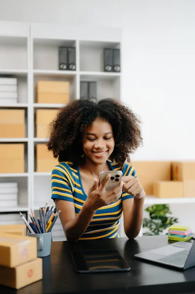 stock image Small business entrepreneur SME freelance African woman working at home office with boxes and laptop with phone, e-commerce concept