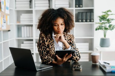 Modern ofiste çalışan tabletli ve bilgisayarlı genç Afrikalı kadın.