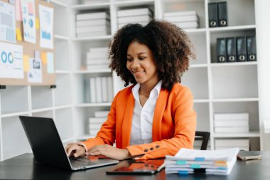 Modern ofiste çalışan tabletli ve bilgisayarlı genç Afrikalı kadın.