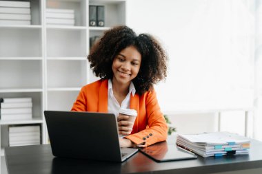 Modern ofiste çalışan tabletli ve bilgisayarlı genç Afrikalı kadın.