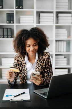 Afrikalı Kadın mobil ödemeler için akıllı telefon kullanıyor online alışveriş, omni kanalı, masada oturuyor, sanal simge grafik arayüzü 
