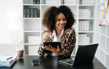 Modern ofiste çalışan tabletli ve bilgisayarlı genç Afrikalı kadın.