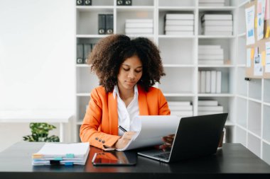 Modern ofiste çalışan tabletli ve bilgisayarlı genç Afrikalı kadın.