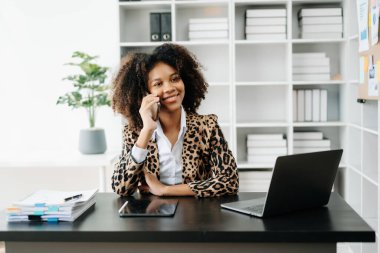 Modern ofiste çalışan telefon, tablet bilgisayar ve bilgisayarlı genç Afrikalı kadın.
