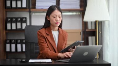 Bir ofis masasında matematik finansmanı, vergi, rapor, muhasebe, istatistik ve analitik araştırma kavramında tablet bilgisayar ve dizüstü bilgisayar kullanan iş kadını