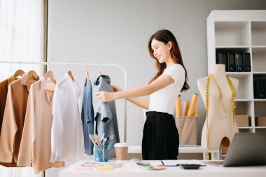 Asyalı moda tasarımcısı kadın terzi galerisinde çalışırken kıyafetlerini kontrol ediyor. 