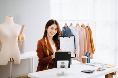 Asyalı terzi kadın elbise atölyesinde çalışıyor. istatistiklerle birlikte görüntülü arama yapmak ve dizini göstermek 