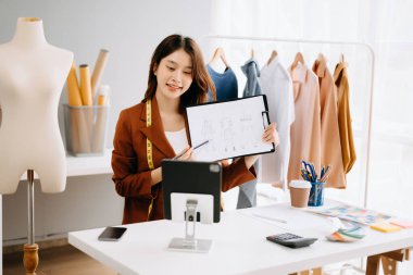 Genç Asyalı terzi kadın terzi atölyesinde giysiler üzerinde çalışıyor. canlı arama yapmak ve dizini istatistiklerle göstermek 