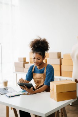 Dijital tablet kullanan Afro-Amerikalı bir kadın. Online alışverişleri kontrol ediyorum. arkaplandaki ürün kutuları 
