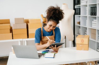 Dijital tablet kullanan Afro-Amerikalı bir kadın. Online alışverişleri kontrol ediyorum. arkaplandaki ürün kutuları 