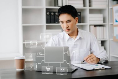  Bilgisayarlı ve akıllı telefonlu Asyalı iş adamı modern ofiste sanal ikon diyagramı ile masa başında çalışıyor. 