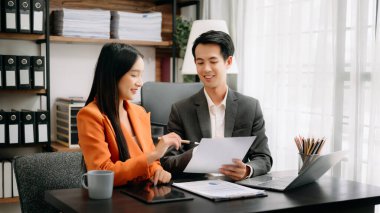 İki Asyalı işadamı, modern ofiste tablet bilgisayar ve dizüstü bilgisayarla çalışma ve planlama stratejisini tartıştı.