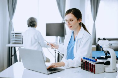 İki bilim adamı ya da tıp teknisyeni, Asyalı kıdemli bir kadın bilim adamıyla çevrimiçi okuma ve test örnekleriyle laboratuarda görüşüyor. 