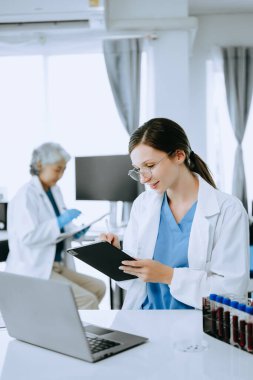İki bilim adamı ya da tıp teknisyeni, Asyalı kıdemli bir kadın bilim adamıyla çevrimiçi okuma ve test örnekleriyle laboratuarda görüşüyor. 