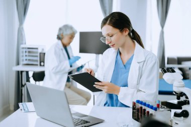 İki bilim adamı ya da tıp teknisyeni, Asyalı kıdemli bir kadın bilim adamıyla çevrimiçi okuma ve test örnekleriyle laboratuarda görüşüyor. 