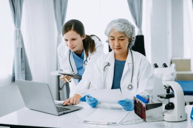 Tıbbi ekip, beyaz laboratuvar önlüklü ve ameliyat önlüklü doktorlarla toplantı yapıyor. Masada oturmuş, internette çalışan hastaları tartışıyorlar. Tıp endüstrisinde bilgisayar kullanıyorlar..