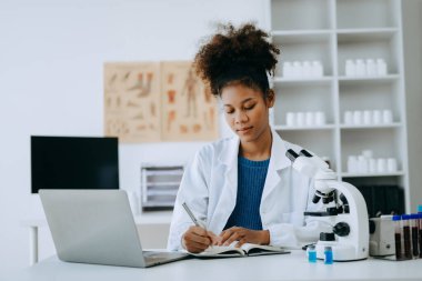 Afrikalı gülümseyen doktor ya da danışman bir masada oturmuş hasta raporu, ameliyat planlaması ve reçete yazıyor.