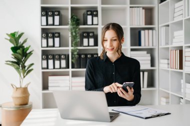 Confident business expert attractive smiling young woman typing laptop ang holding digital tablet on desk in creative office