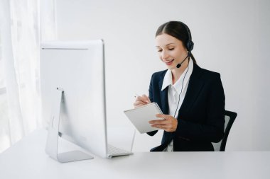 Kablosuz kulaklıkla çağrı merkezi operatörü müşteriyle konuşuyor ve notlar yazıyor, mikrofonlu bir kadın bilgisayar monitörüyle çalışırken danışmanlık yapıyor. 