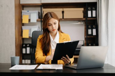 Ofiste çalışan Asyalı bir iş kadını. Not defteri, tablet ve dizüstü bilgisayarla ofiste çalışıyor.