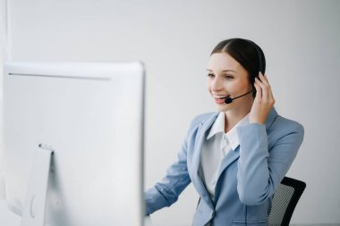 Kablosuz kulaklıkla çağrı merkezi operatörü. Müşteri ile konuşuyor. Kulaklıklı kadın, bilgisayar monitörüyle masada çalışırken mikrofon danışmanlığı yapıyor. 