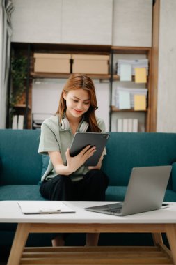 Bayan öğrenciler, Asyalı kız kütüphanesindeki kitaplardan dizüstü bilgisayar ve tabletle internet bilgilerini arayarak koltukta oturuyorlar. Oturma odasında.