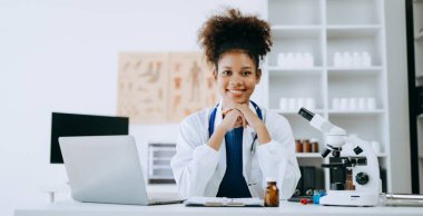 Afrikalı gülümseyen doktor ya da danışman bir masada oturmuş hasta raporu, ameliyat planlaması ve reçete yazıyor.