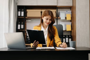 Ofiste çalışan Asyalı bir iş kadını. Not defteri, tablet ve dizüstü bilgisayarla ofiste çalışıyor.