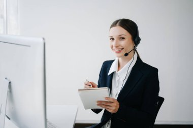 Kablosuz kulaklıkla çağrı merkezi operatörü müşteriyle konuşuyor ve notlar yazıyor, mikrofonlu bir kadın bilgisayar monitörüyle çalışırken danışmanlık yapıyor. 