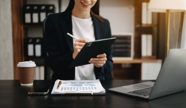 Bilgisayarda, tablette ve modern ofisindeki iş yerinde çalışan kendinden emin bir iş kadını.