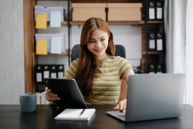 İş kadını Asyalı kadın telefonda konuşuyor ve evinde otururken bilgisayarını gülümsüyor.