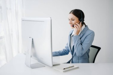 Kablosuz kulaklıkla çağrı merkezi operatörü. Müşteri ile konuşuyor. Kulaklıklı kadın, bilgisayar monitörüyle masada çalışırken mikrofon danışmanlığı yapıyor. 