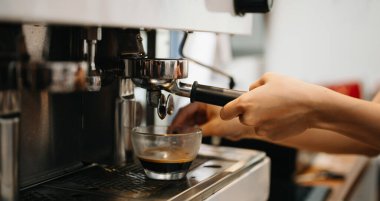 Profesyonel espresso makinesi cam bardağa taze kahve dolduruyor.