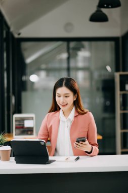 Çalışan beyaz masa ofisinde oturan genç, güzel Asyalı kadın masaya yazı yazıyor.
