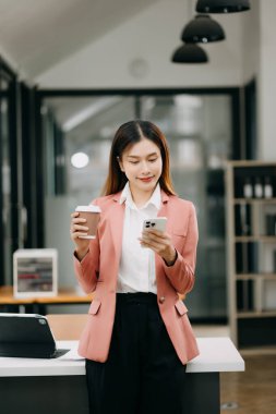 Modern ofiste akıllı telefon kullanan kendine güvenen Asyalı kadın.