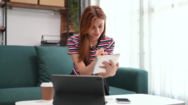 Jovem Bela Mulher Fazendo Anotações Com Tablet Digital Enquanto Senta — Vídeo de Stock