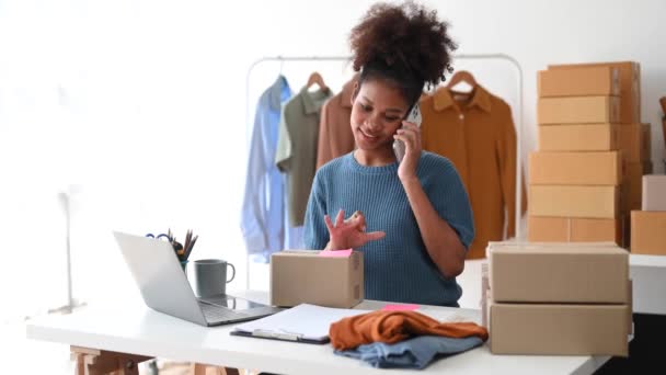 创业的中小企业 企业主非洲妇女使用智能手机或平板电脑接收和检查网上购物订单 准备包装产品盒 — 图库视频影像