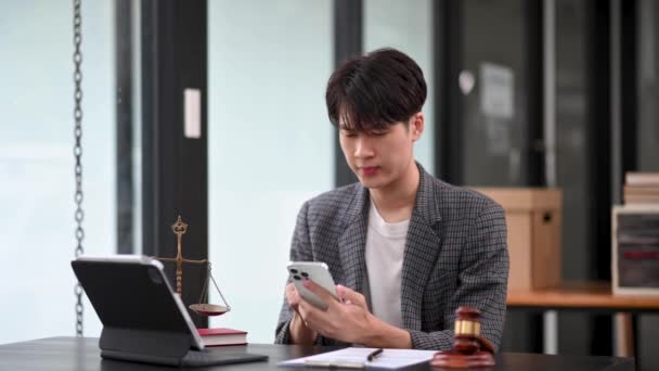 スマートフォンでオフィスで働くハンサムなアジア人男性弁護士 アドバイス 正義と法律コンセプト — ストック動画