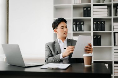 Modern ofiste çalışan genç Asyalı işadamı dizüstü bilgisayarı, tableti ve kâğıdı not alıyor.