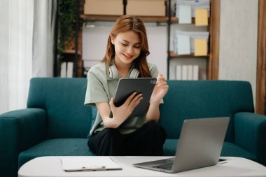 Kanepede oturan kız öğrenci, oturma odasındaki online bilgileri aramak için tablet bilgisayar kullanıyor.