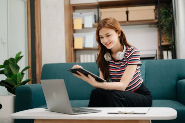 Kanepede oturan kız öğrenci, oturma odasındaki online bilgileri aramak için tablet bilgisayar kullanıyor.