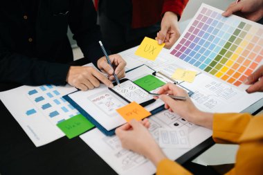 UX geliştiricisi ve ui tasarımcıları modern ofiste müşteri özeti ve renk kodu ile mobil uygulama arayüzü kablo tasarımı hakkında beyin fırtınası yapıyorlar.