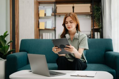 Bayan öğrenciler, Asyalı kız kütüphanesindeki kitaplardan dizüstü bilgisayar ve tabletle internet bilgilerini arayarak koltukta oturuyorlar. Oturma odasında.