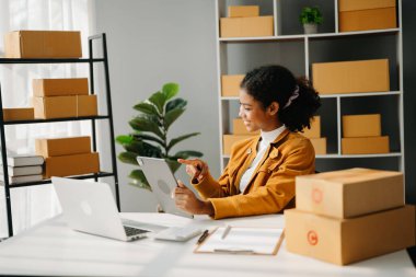 Başlangıçta küçük işletme KOBİ 'si, Girişimci sahibi Afrikalı kadın paket ürün kutularını hazırlamak için online alışveriş siparişlerini alıyor ve kontrol ediyor. Merkez ofiste.