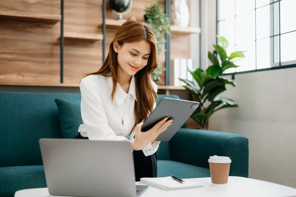 stock image Businesswoman using tablet and laptop for doing math finance, tax, report, accounting, statistics, and analytical research concept on sofa at home office