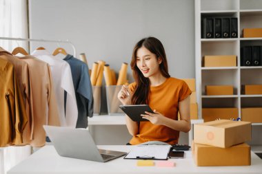 Moda blogcusu kavramı, giysi satan genç Asyalı kadın. Akıllı telefon ve dizüstü bilgisayar kullanarak küçük işletme KOBİ 'si kurun, ofiste satın alın ve kontrol edin