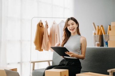 Genç işyeri sahibi kadın paket kutusunu hazırla ve tablet, dizüstü bilgisayar alışverişi online konsept üzerinden müşteriye teslimat için çevrimiçi kontrol yap